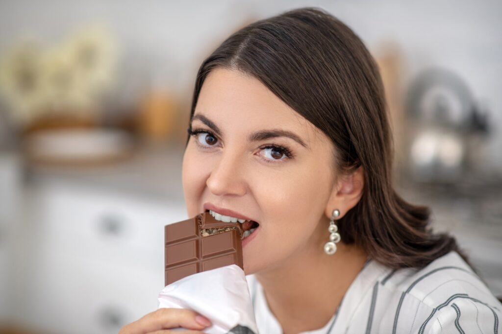 Dark-haired woman in a striped blouse eating chocolate